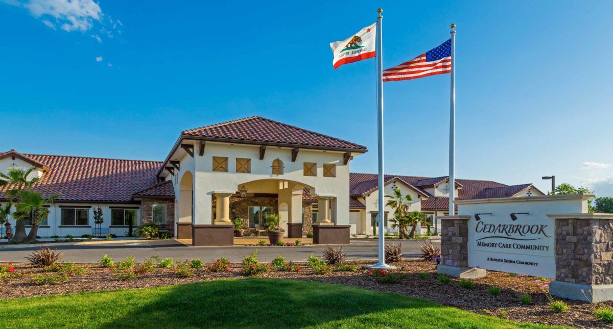 A building with California and U.S. flags waving in front under a clear blue sky.