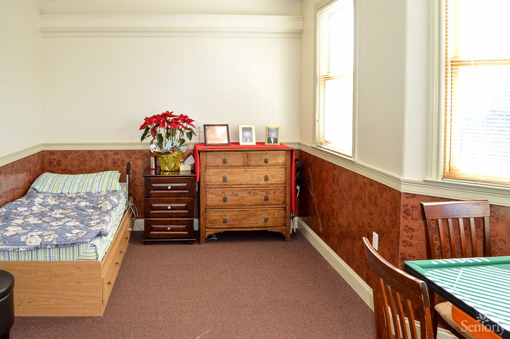A cozy bedroom with a bed, dresser, and window, featuring a plant and wooden furniture.