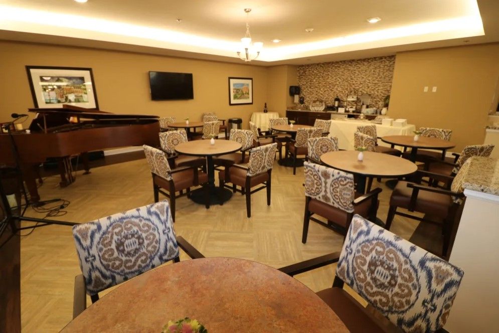 A cozy dining area with tables, chairs, a piano, and a buffet setup.