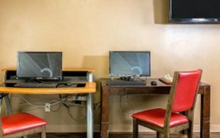 A small office setup with two computers on separate desks, each accompanied by a red chair.