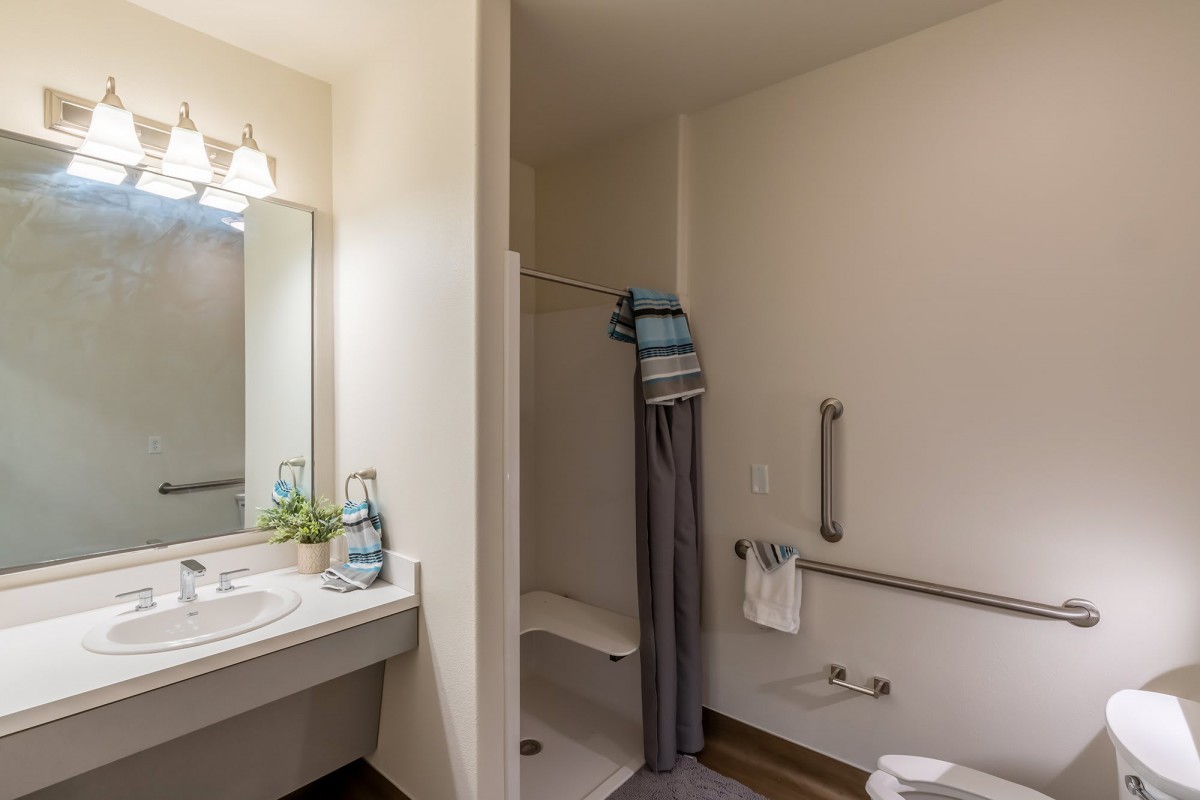 An accessible bathroom featuring a shower with a grab bar, a sink with a mirror, and neatly arranged towels.