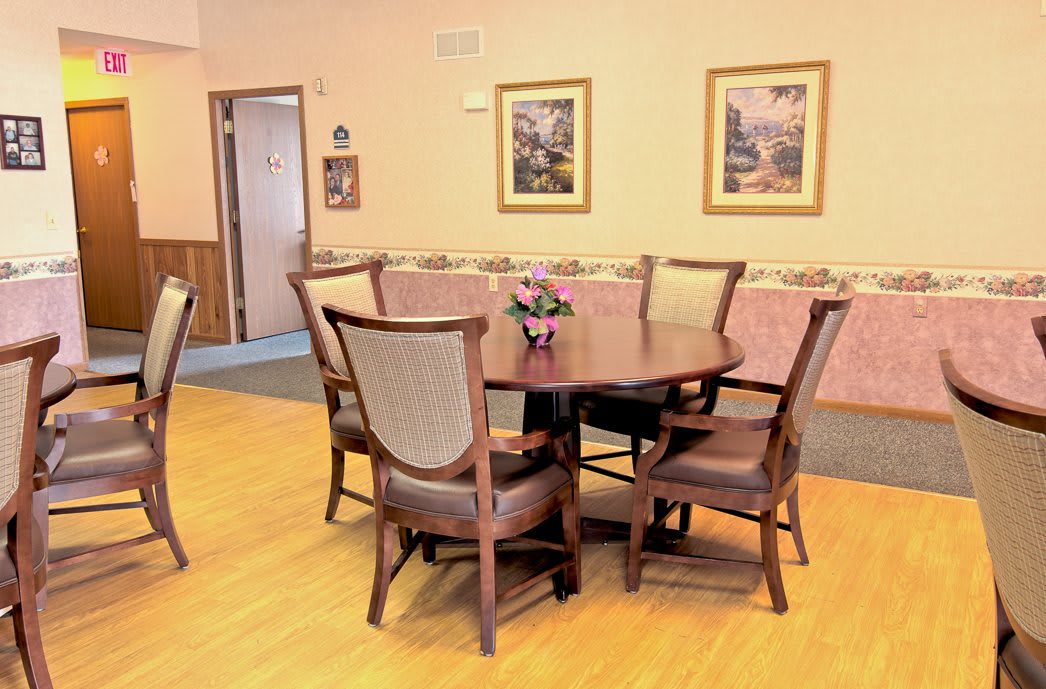 A cozy dining room with a round table and six chairs, adorned with paintings on the walls.