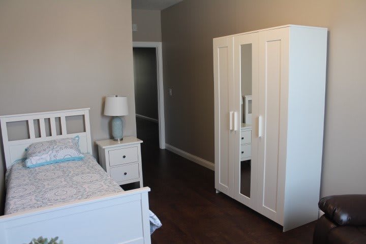 A cozy bedroom with a white wardrobe, nightstand, and bed.