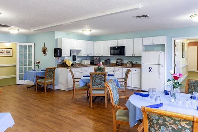 A cozy dining area with round tables set for meals, adjacent to a kitchen with white cabinets.