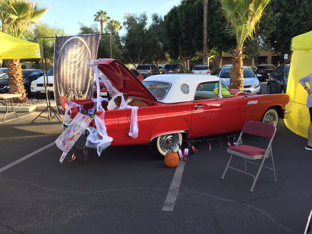 A classic red car decorated for Halloween with cobwebs and a pumpkin in a parking lot.