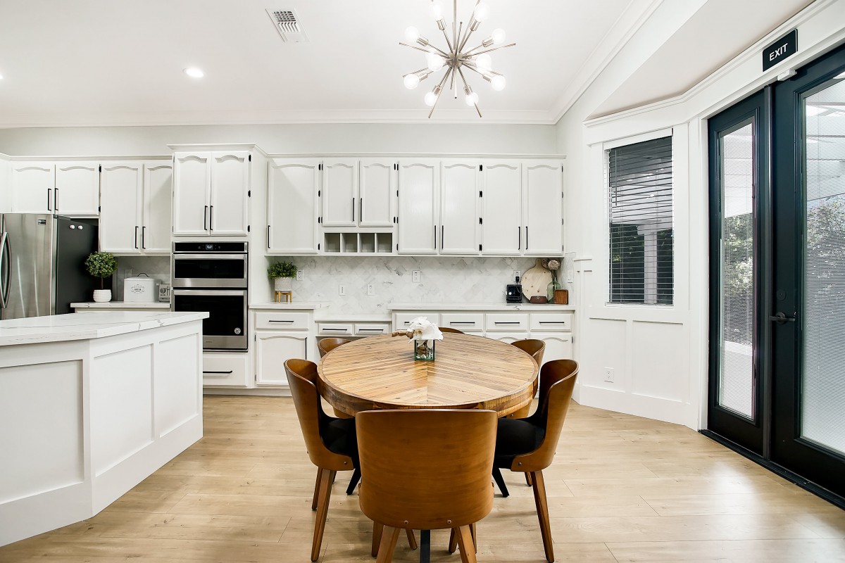 A modern kitchen with white cabinets, a round wooden dining table, and stylish lighting.