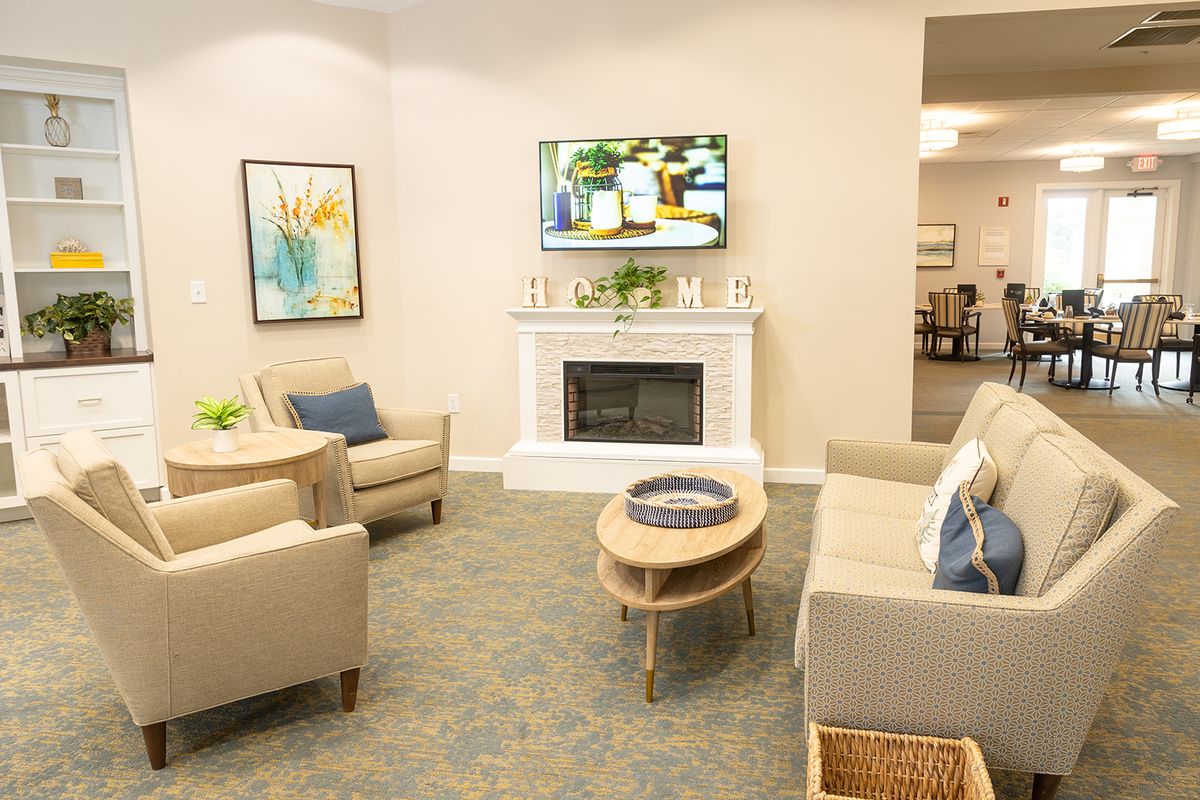 A cozy living room with modern furniture, including sofas and armchairs arranged around a coffee table in front of a fireplace and television.