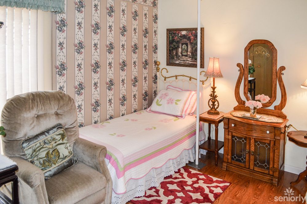 A cozy vintage-themed bedroom with patterned wallpaper, a single bed, and antique furniture.