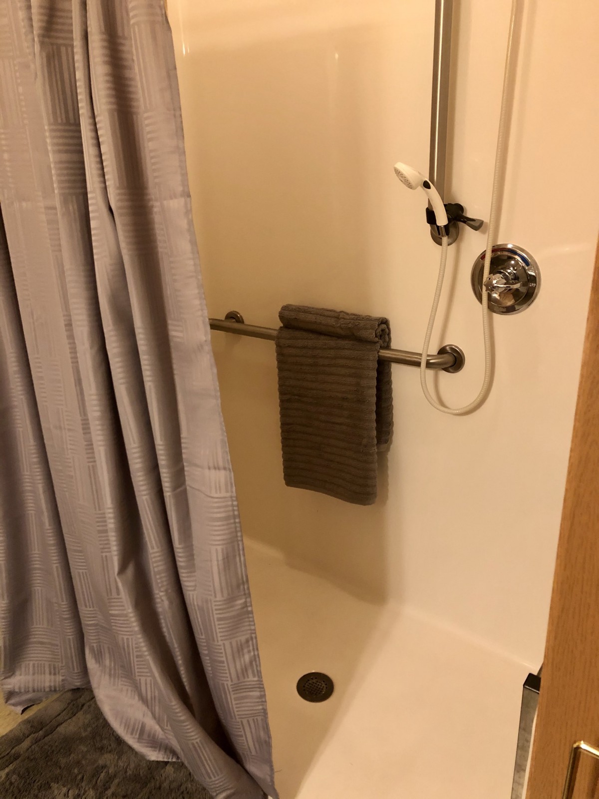 A bathroom shower with a curtain, handrail, and towel hanging.