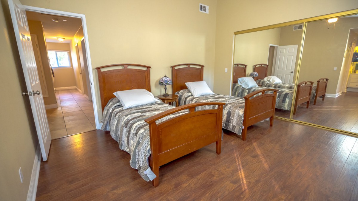 A neatly arranged bedroom featuring two twin beds with striped bedding and wooden frames, complemented by a nightstand and mirror.