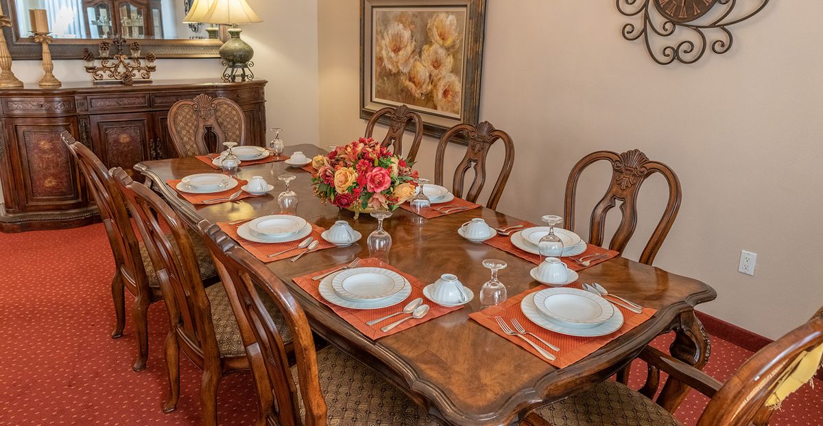 A beautifully set dining table with elegant dinnerware, a floral centerpiece, and warm interior lighting.