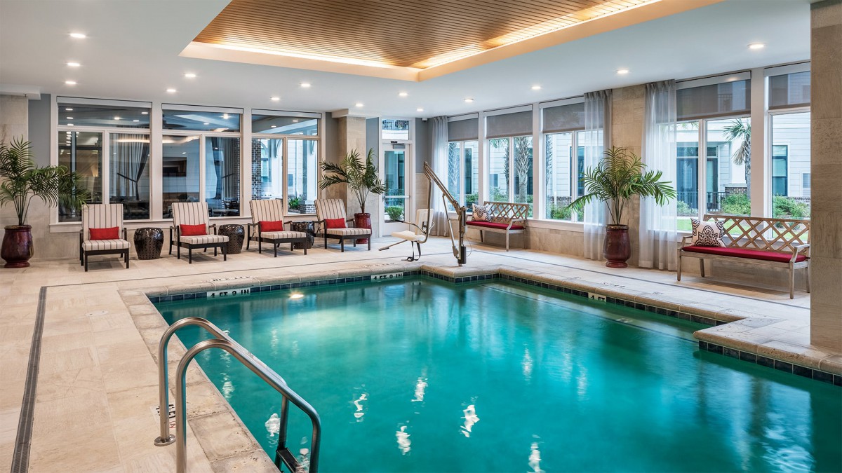 A modern indoor swimming pool area with lounge chairs and plants.