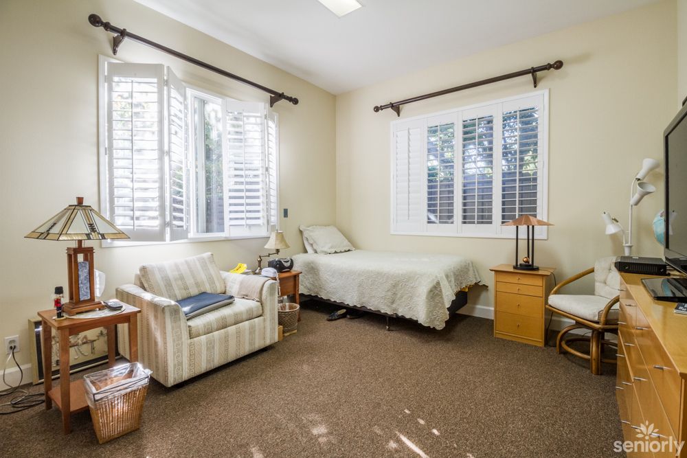 A cozy bedroom with a single bed, an armchair, and natural light coming through the windows.