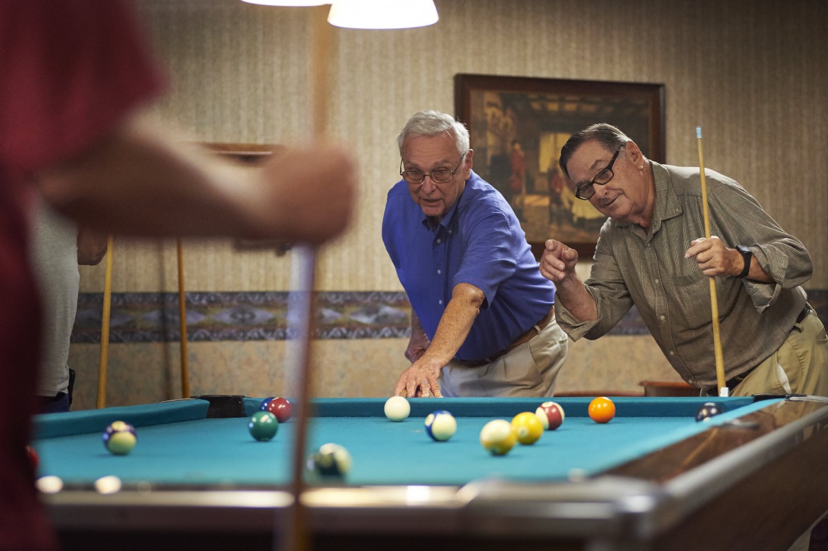 Two men playing billiards on a pool table indoors.