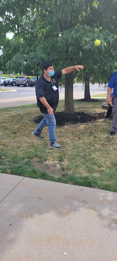 A man wearing a mask is walking on the grass near a tree.