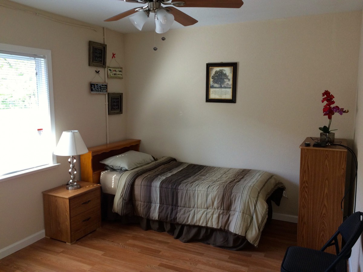 A simple bedroom with a single bed, nightstand, and ceiling fan.