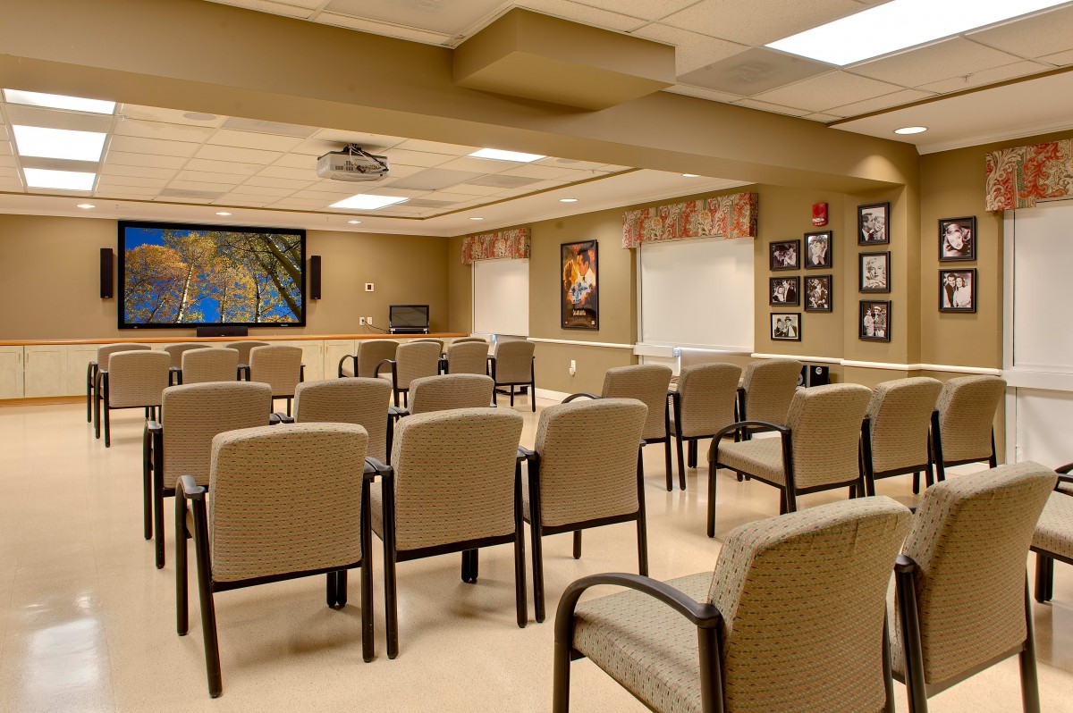 An empty conference room with arranged chairs and a projector screen at the front.