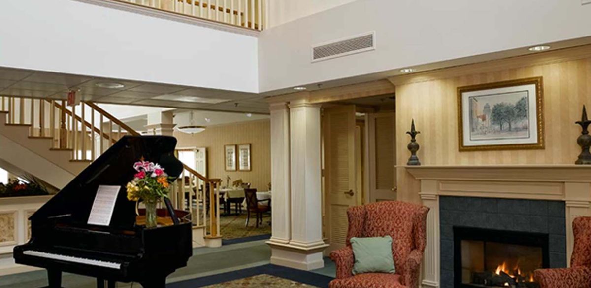 A cozy lobby interior with an armchair, piano, and floral arrangement.