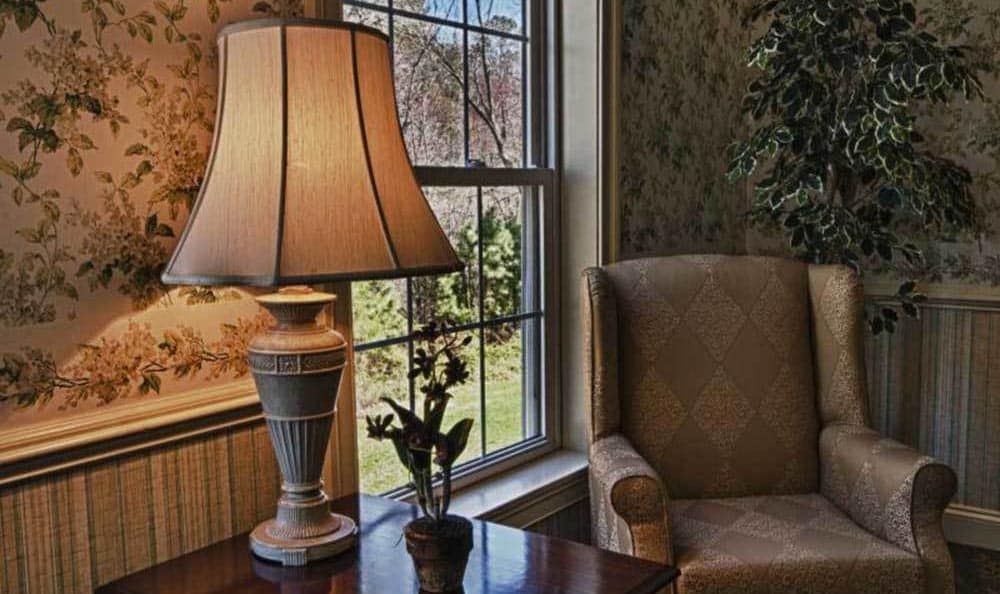 A cozy corner featuring a lamp, armchair, and window with a small plant on the table.
