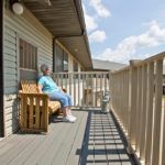 A person sits on a bench enjoying a sunny day on a porch.
