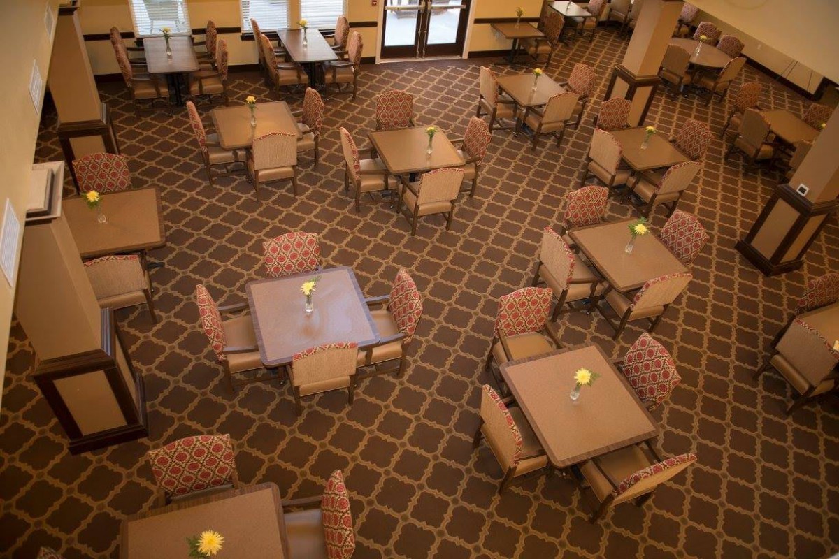 An empty dining room with neatly arranged tables and chairs on a carpeted floor.