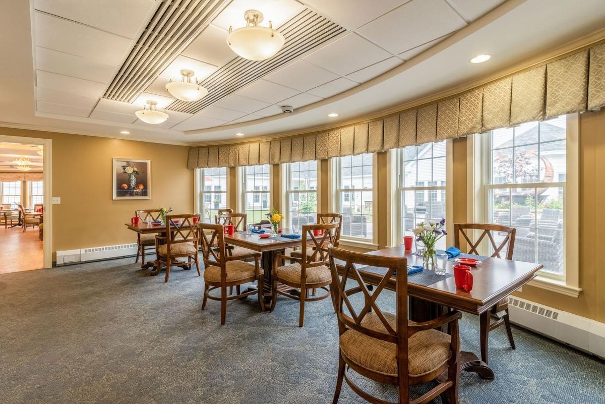A well-lit dining room with multiple tables and chairs, featuring large windows that provide ample natural light.