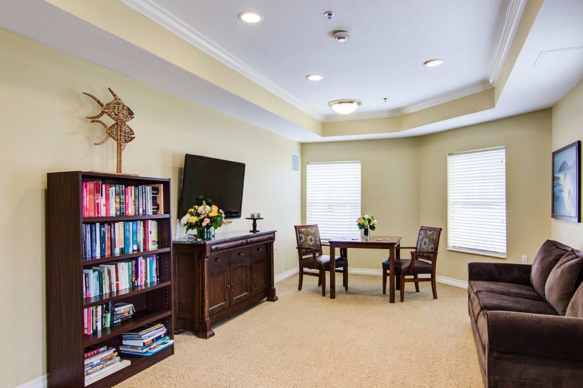 A cozy living room featuring a bookshelf, wall-mounted television, and a small dining table with chairs.