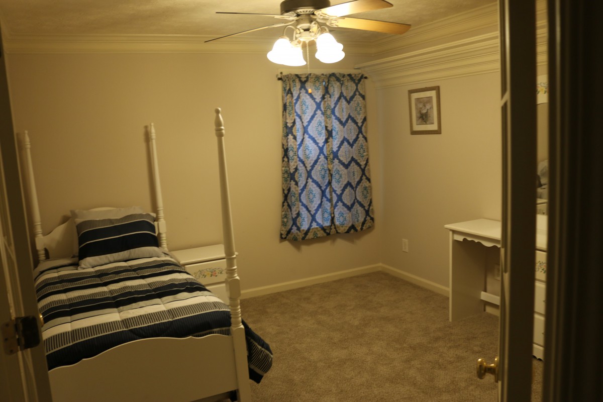 A cozy bedroom with bunk beds and a small desk, featuring a ceiling fan and patterned curtains.