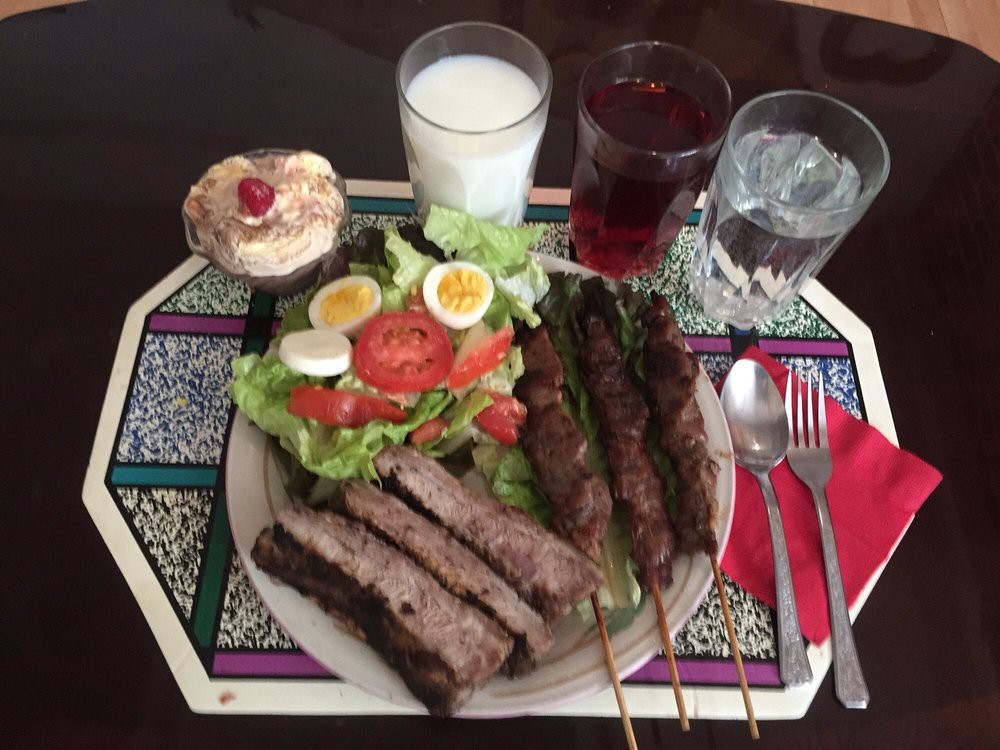 A meal featuring grilled meat skewers, a fresh salad with boiled eggs, rye bread, and assorted drinks including milk and juice.