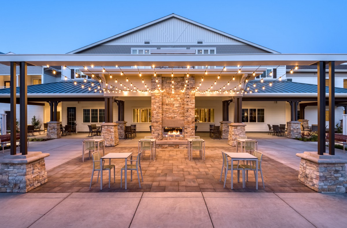 An inviting outdoor patio with string lights and a central fireplace, surrounded by tables and chairs in the evening.