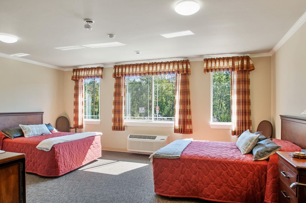 A spacious hotel room with two beds, large windows, and ample natural light.