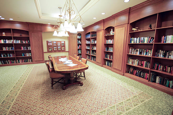 A cozy library room with wooden bookshelves, a central table, and warm lighting.