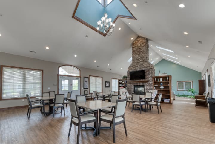 A spacious dining area with modern decor, featuring a high ceiling, chandelier, and cozy fireplace.