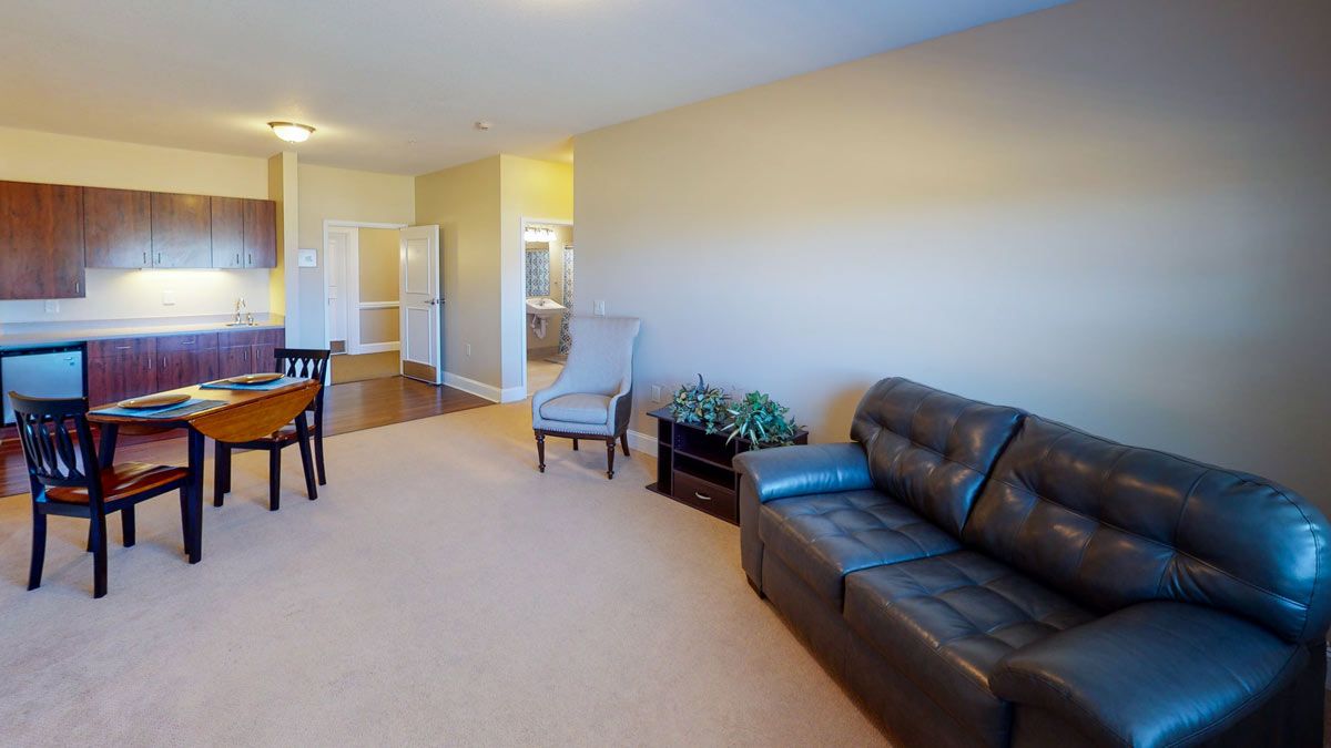 A cozy living room with a sofa, armchair, and dining area in the background.