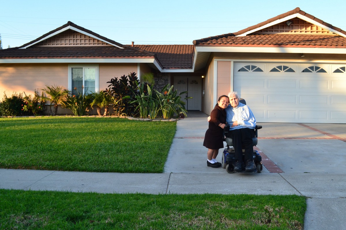 Two people in front of a house, one in a wheelchair, enjoying the sunset.