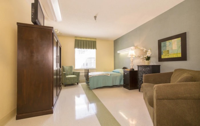 A clean and neatly arranged hospital room with a single bed, armchair, and window.