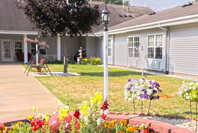 A well-maintained yard with colorful flowers and a classic lamp post in front of a house.