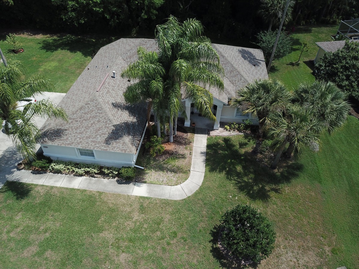 Aerial view of a residential house surrounded by trees and a well-maintained yard.