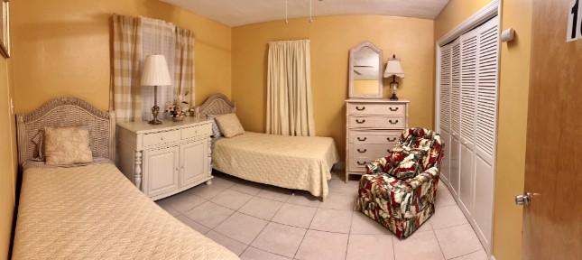 A cozy bedroom with twin beds, a dresser, and a floral armchair.