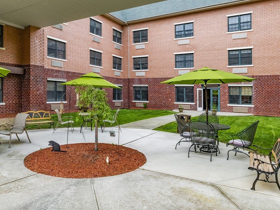 A tranquil courtyard with outdoor seating and green umbrellas next to a brick building.