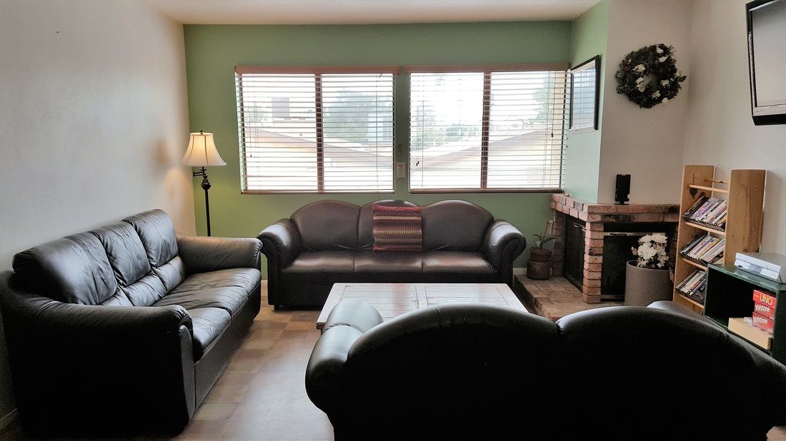 A cozy living room with two sofas, a coffee table, and a fireplace, illuminated by natural light from the windows.