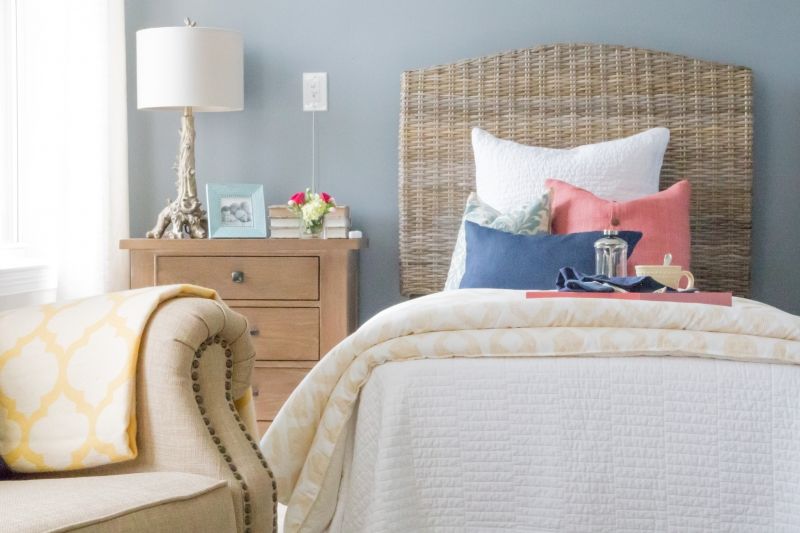 A cozy and stylishly decorated bedroom with a neatly made bed, pillows in various colors, a nightstand with a lamp, and decorative items.