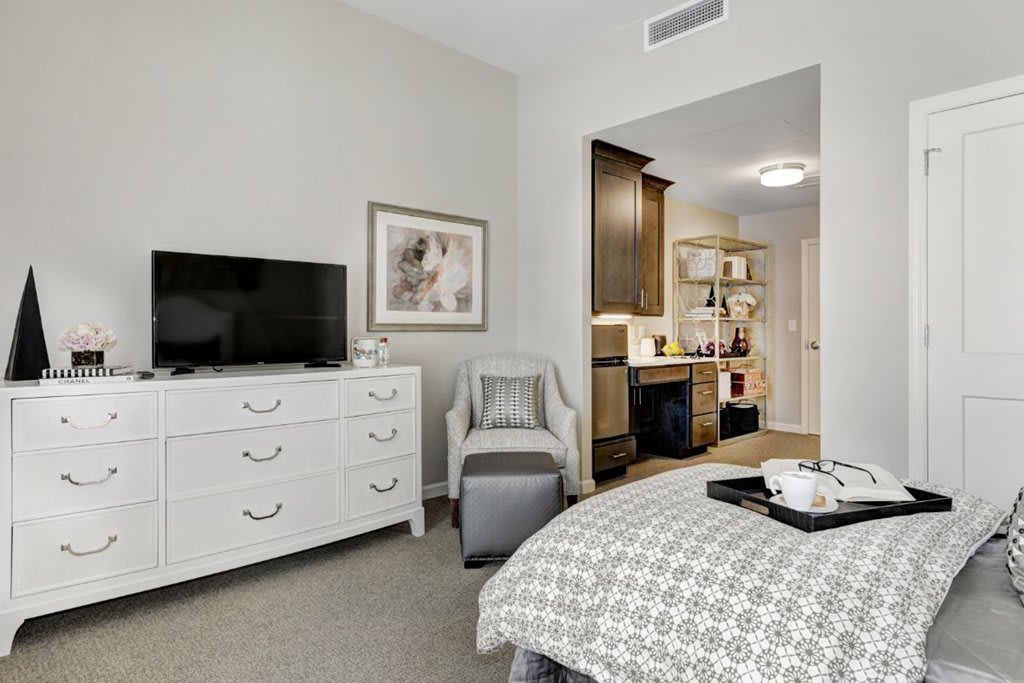 A cozy bedroom featuring a TV on a dresser, a comfortable chair, and neatly decorated neutral tones.
