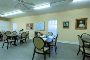 A classroom with tables and chairs, featuring a whiteboard and a ceiling fan.