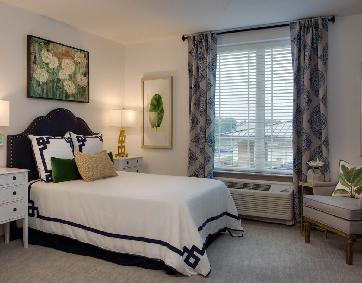 A cozy bedroom with elegant decor, featuring a bed, artwork on the walls, and a large window with curtains.