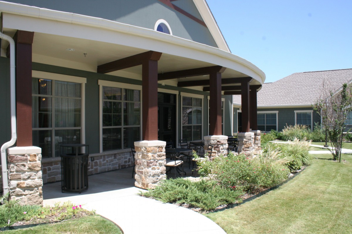 A residential house with a covered porch featuring stone columns and landscaped surroundings.