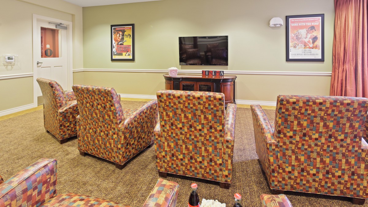 A cozy living room with patterned armchairs facing a television and decorated with wall art.