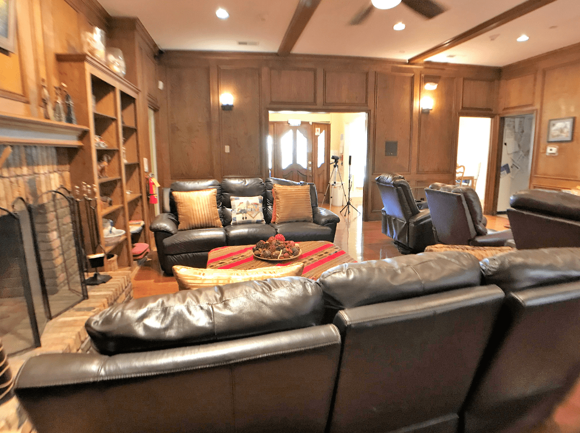 A cozy living room with leather sofas and wood-paneled walls featuring bookshelves.