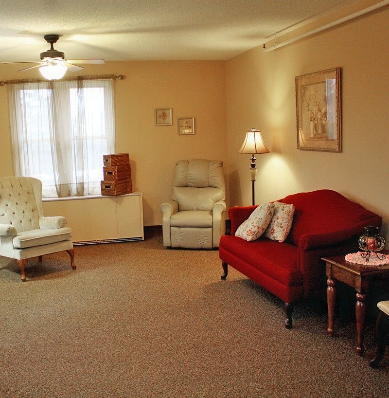 A cozy living room with a red sofa, two armchairs, and a warm lamp.
