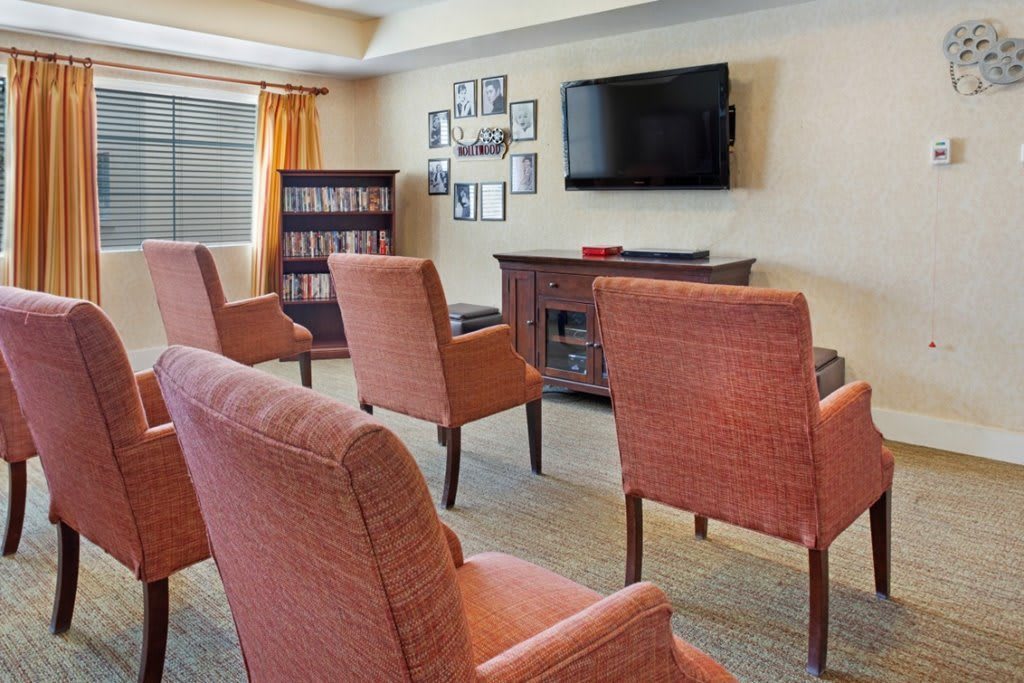 A cozy living room with multiple chairs facing a television and a bookshelf in the corner.